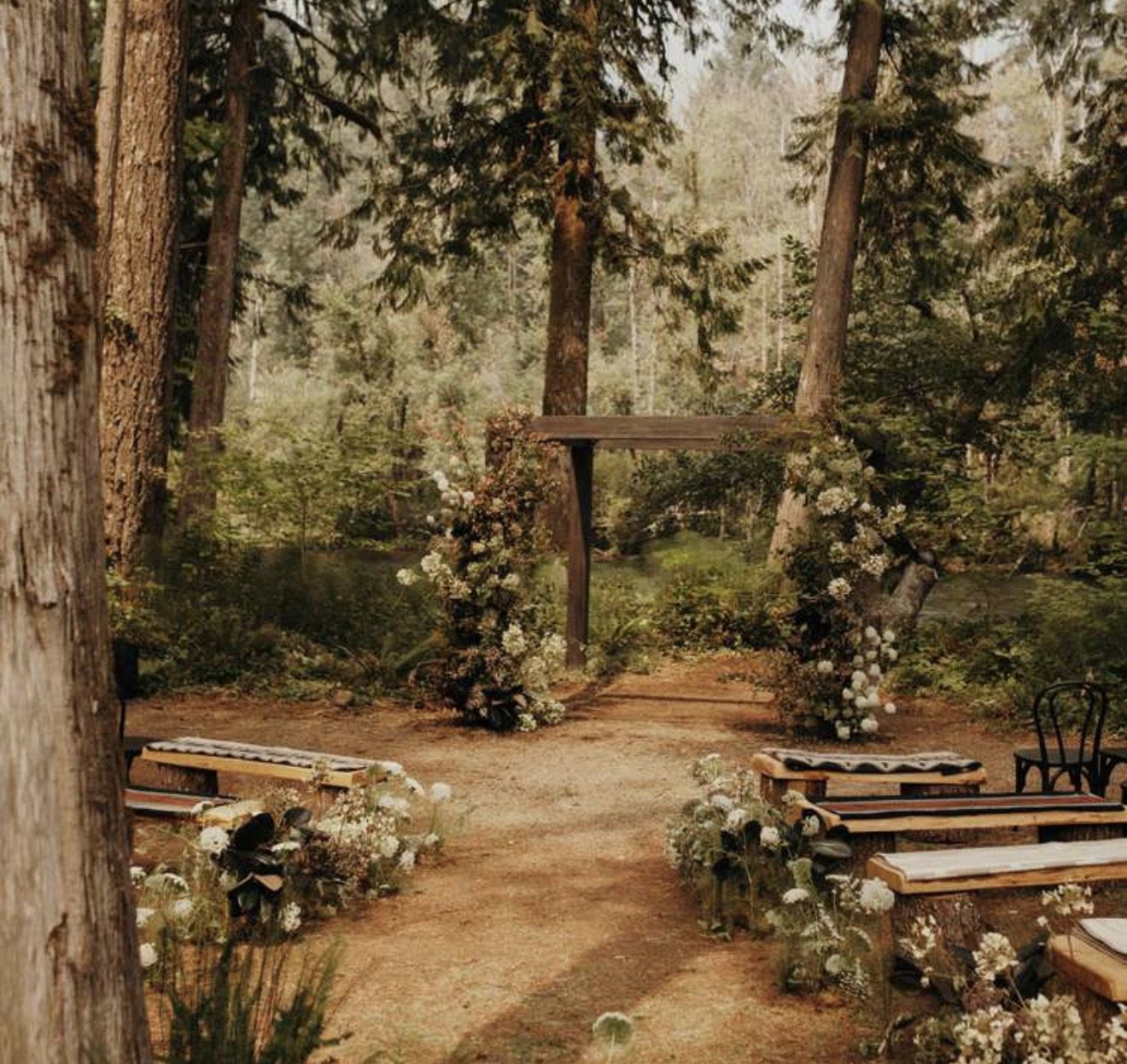 Rustic outdoor wedding ceremony setup in a forest clearing with wooden benches and floral decorations.