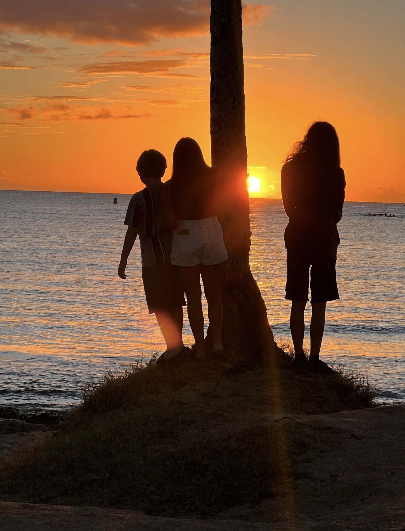 Three people watching a sunset by the water.