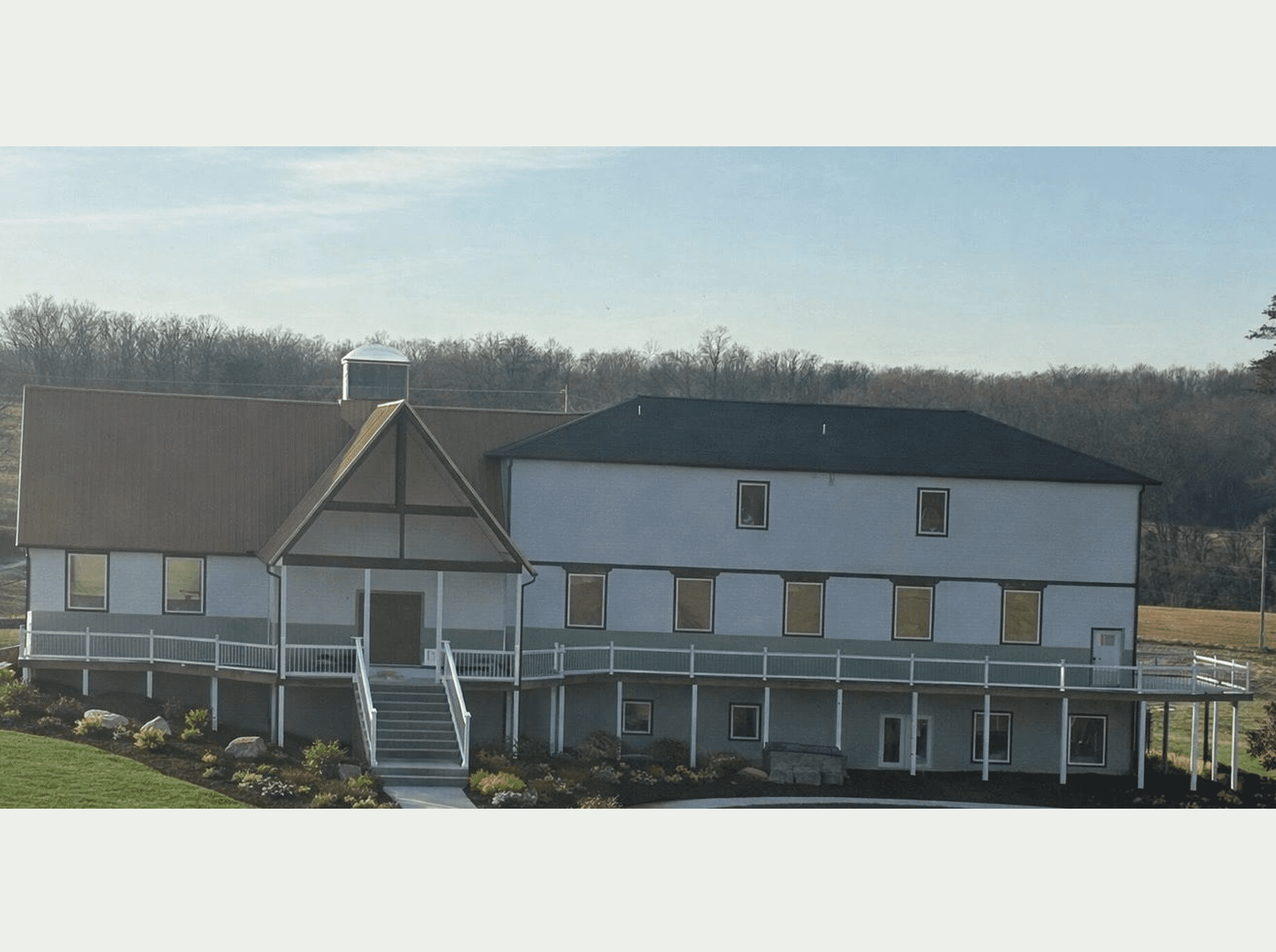 A countryside house with a wrap-around porch under a cloudy sky.