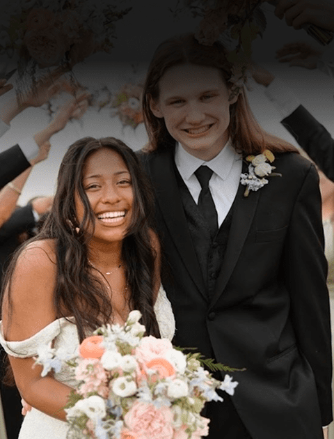 A joyful couple dressed for a wedding, smiling and holding flowers.